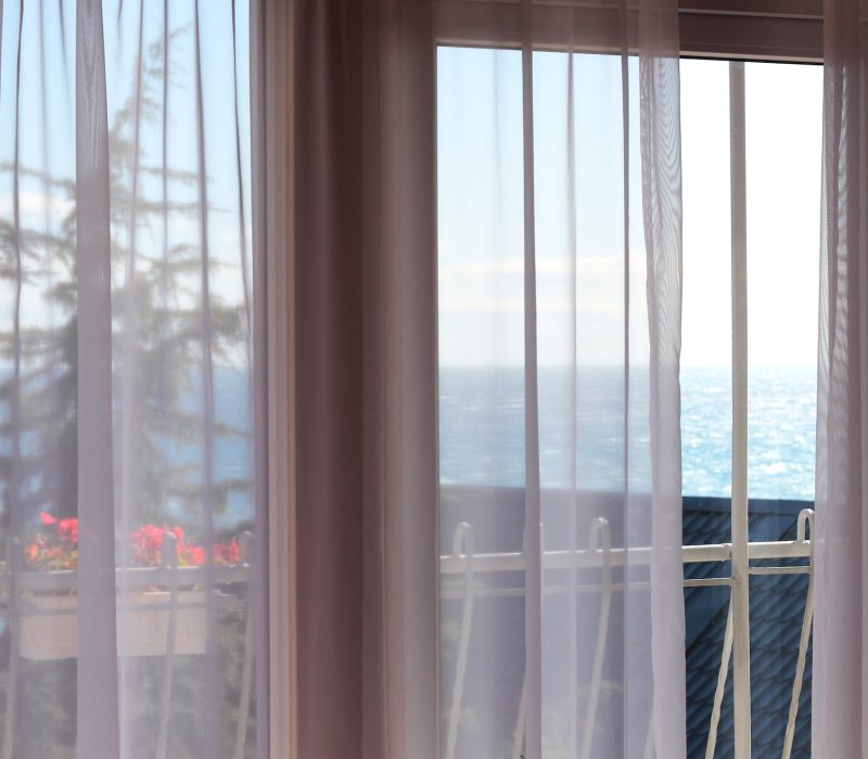 Window and curtains with view of sea in hotel room.